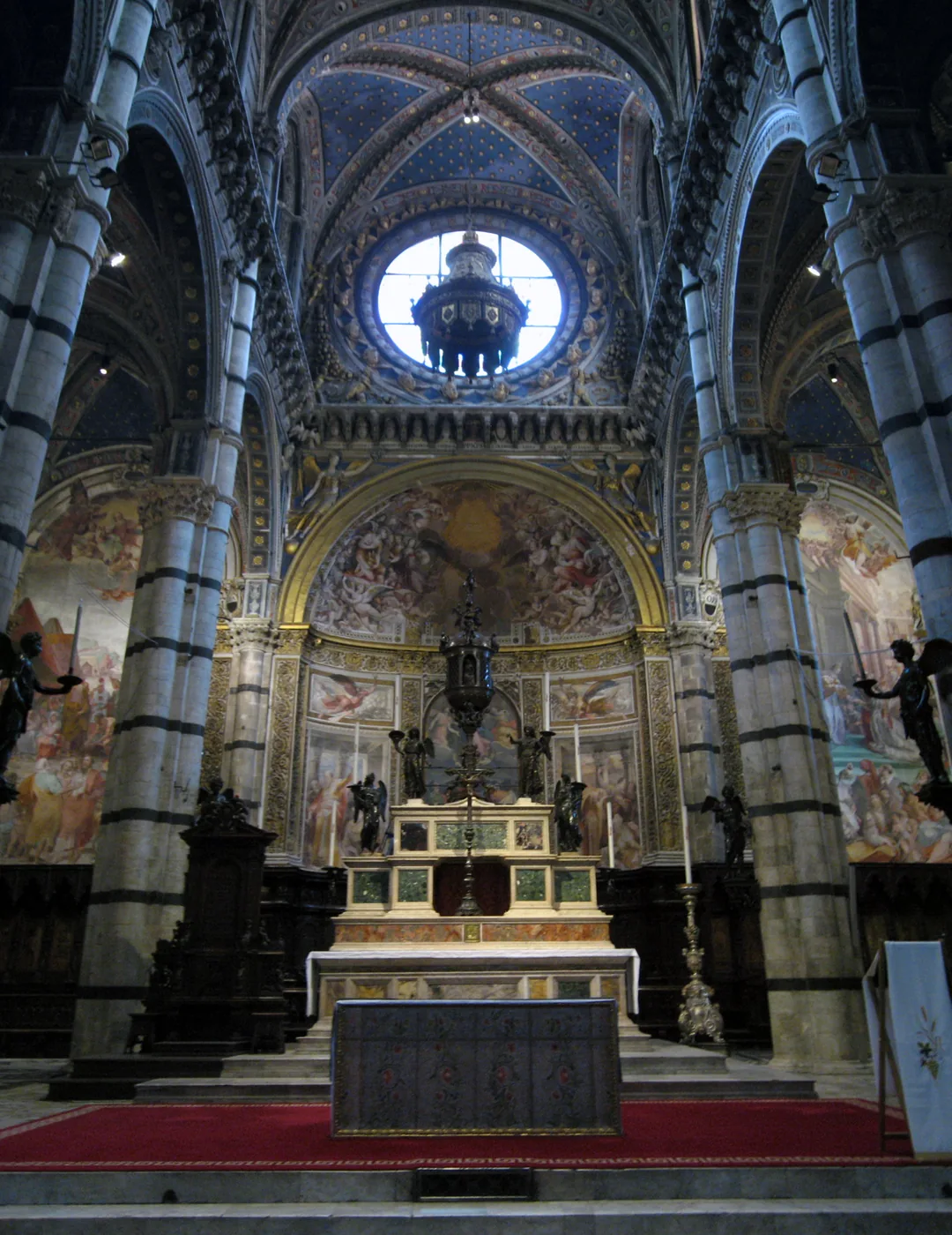 Interior of Siena Cathedral with striped marble columns and frescoed apse