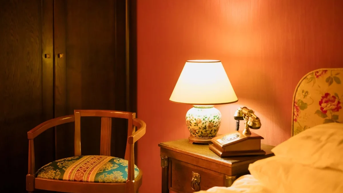 A warmly lit hotel room with a bedside lamp, armchair and vintage telephone