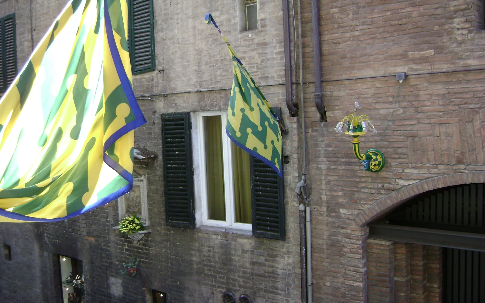 Colourful Contrada del Bruco flags hanging along a historic street in Siena